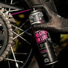 Gloved hand applying Muc-Off All-Weather Chain Lube to a motorcycle chain