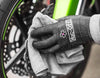 Gloved hand polishing a motorcycle wheel with a grey Muc-Off microfibre cloth